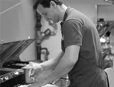 A dedicated chef at Delish Pizza prepares a fresh pizza, showing culinary passion and craftsmanship.